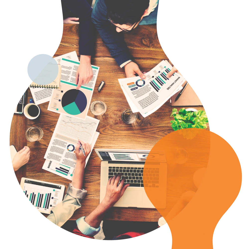 abstract research hub -a diverse team collaborating around a wooden table filled with charts, a laptop, and coffee, framed within a lightbulb-shaped graphic