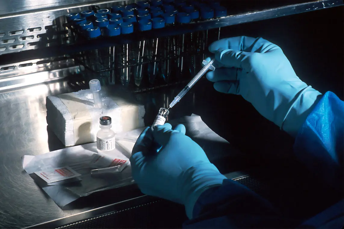 Scientist in blue gloves preparing a syringe from a vaccine vial in a laboratory.